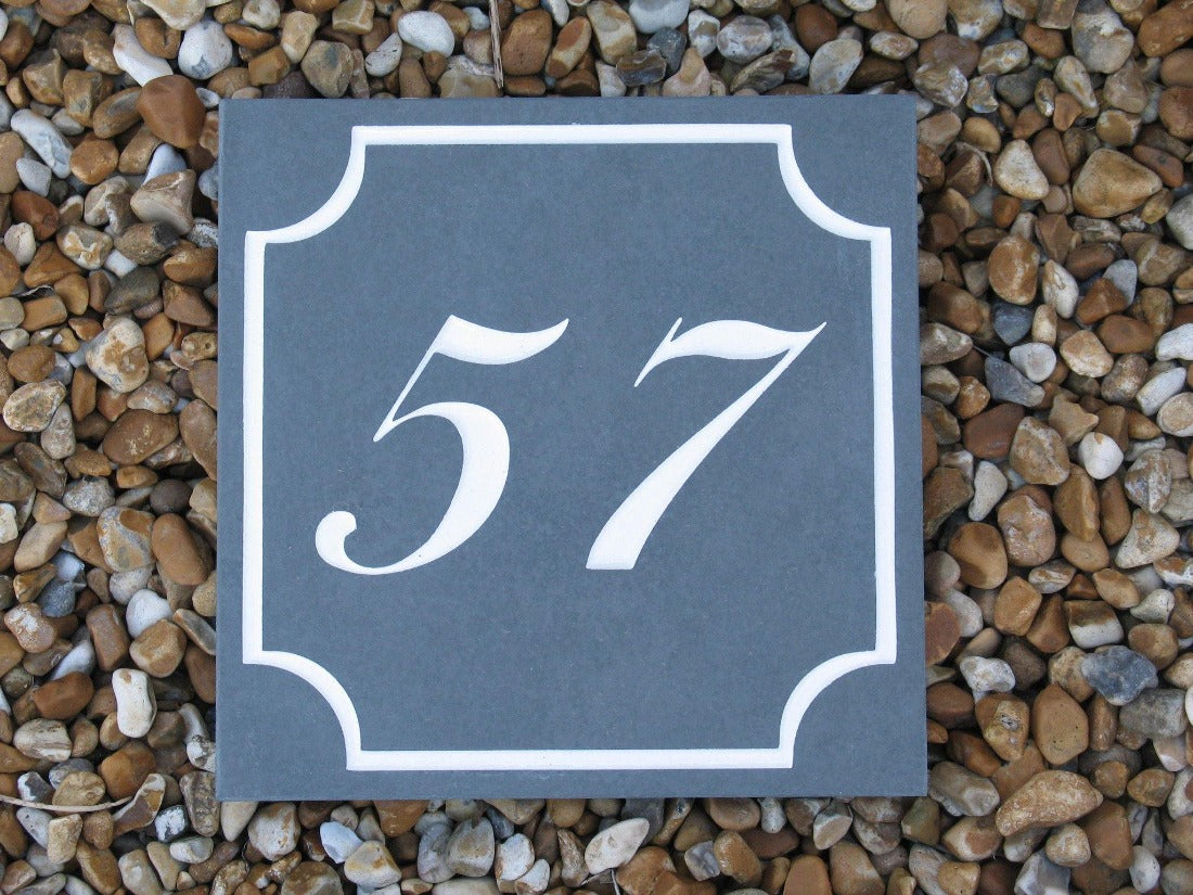 A slate house sign, measuring 150mm x 150mm with a scalloped border, with 15 engraved on charcoal slate, with white paint. Complete with house number 57
