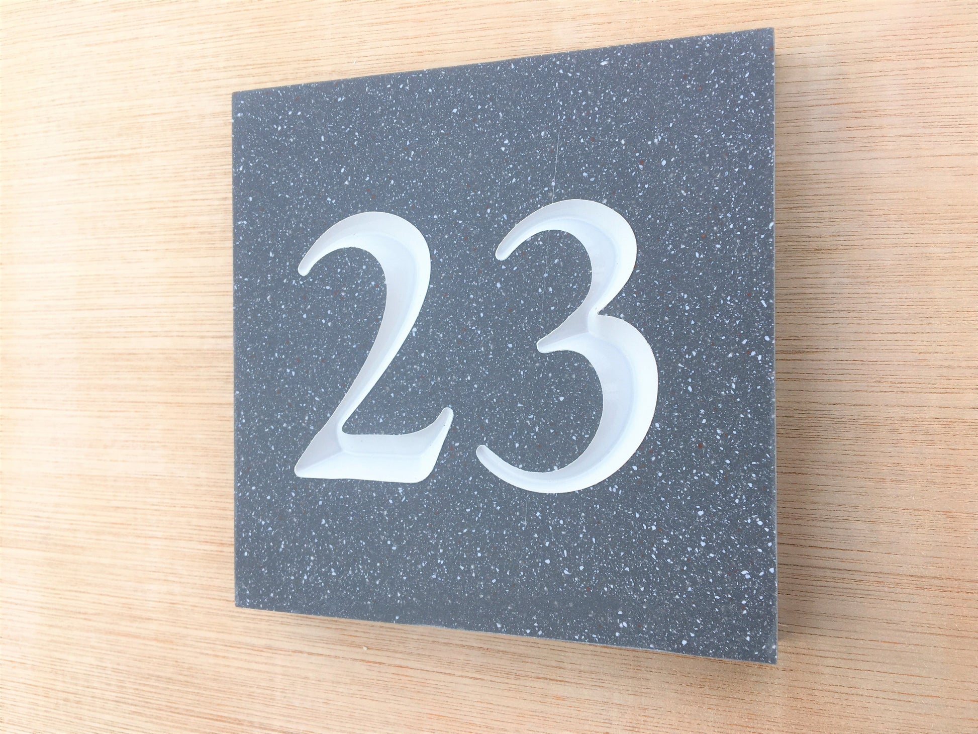 side picture of House sign measuring 100mm x 100mm using grey Corian with the house number 23 deep engraved and infilled with white monument paint