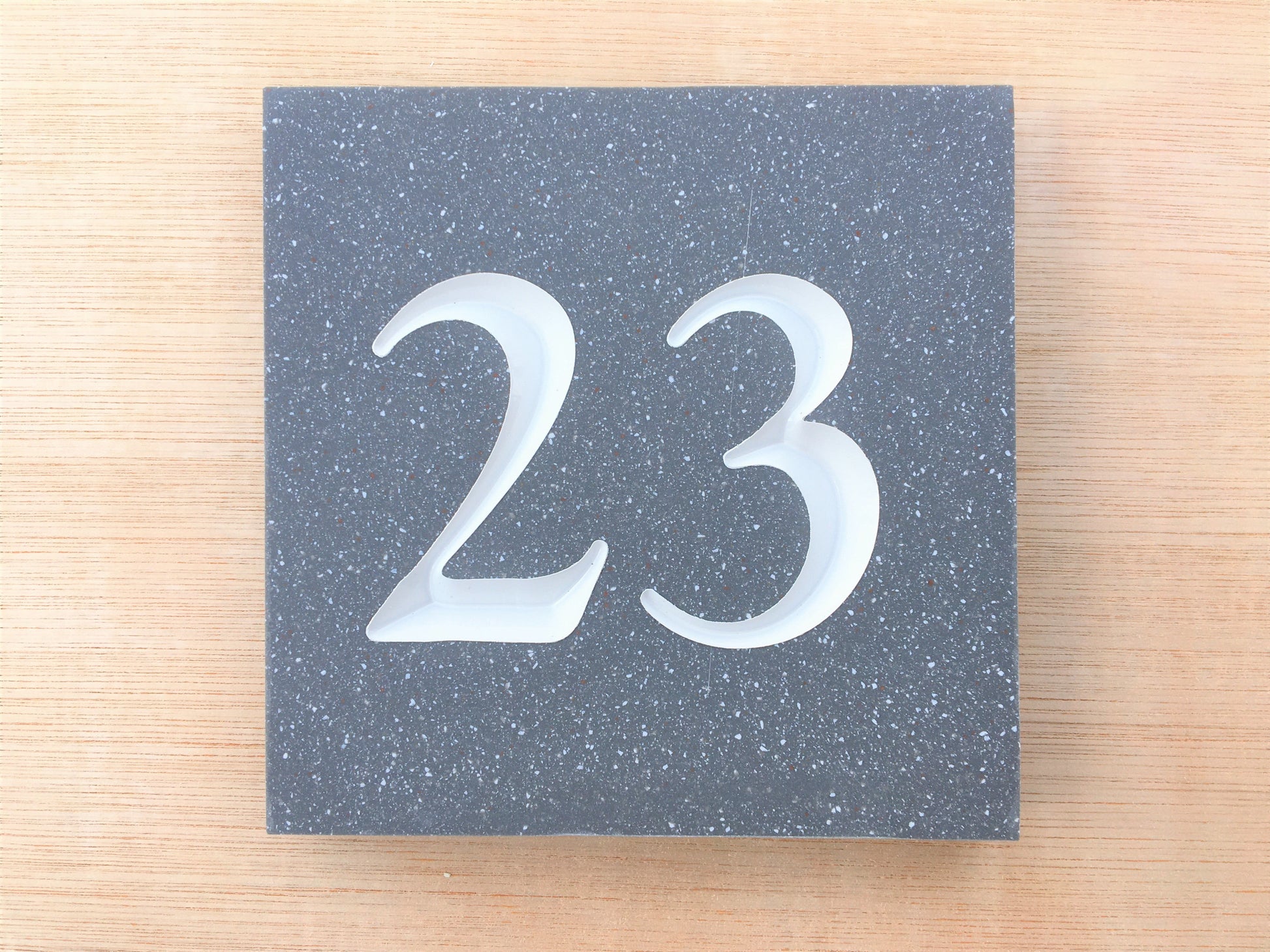 House sign measuring 100mm x 100mm using grey Corian with the house number 23 deep engraved and infilled with white monument paint