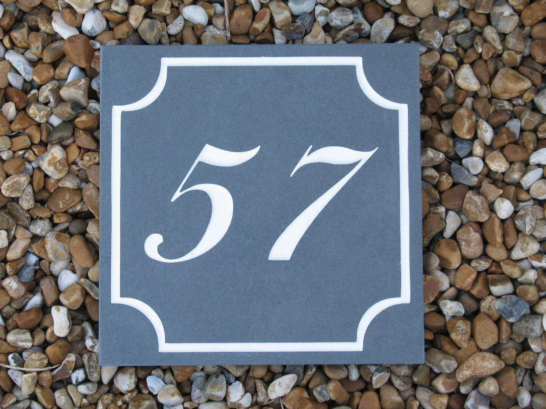 A slate house sign, measuring 150mm x 150mm with a scalloped border, with 15 engraved on charcoal slate, with white paint. Complete with house number 57 