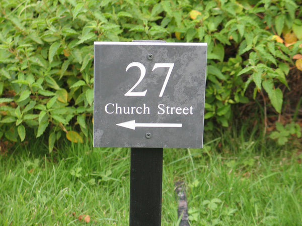 A slate house sign, measuring 200mm x 200mm, deep-engraved house name in Times New Roman font, on grey slate, enhanced with white paint. It is mounted on a wooden post.