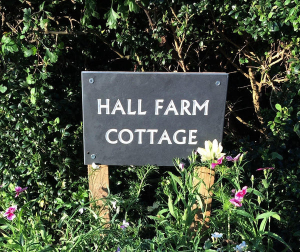 A grey slate sign on posts displaying "Hall Farm Cottage".